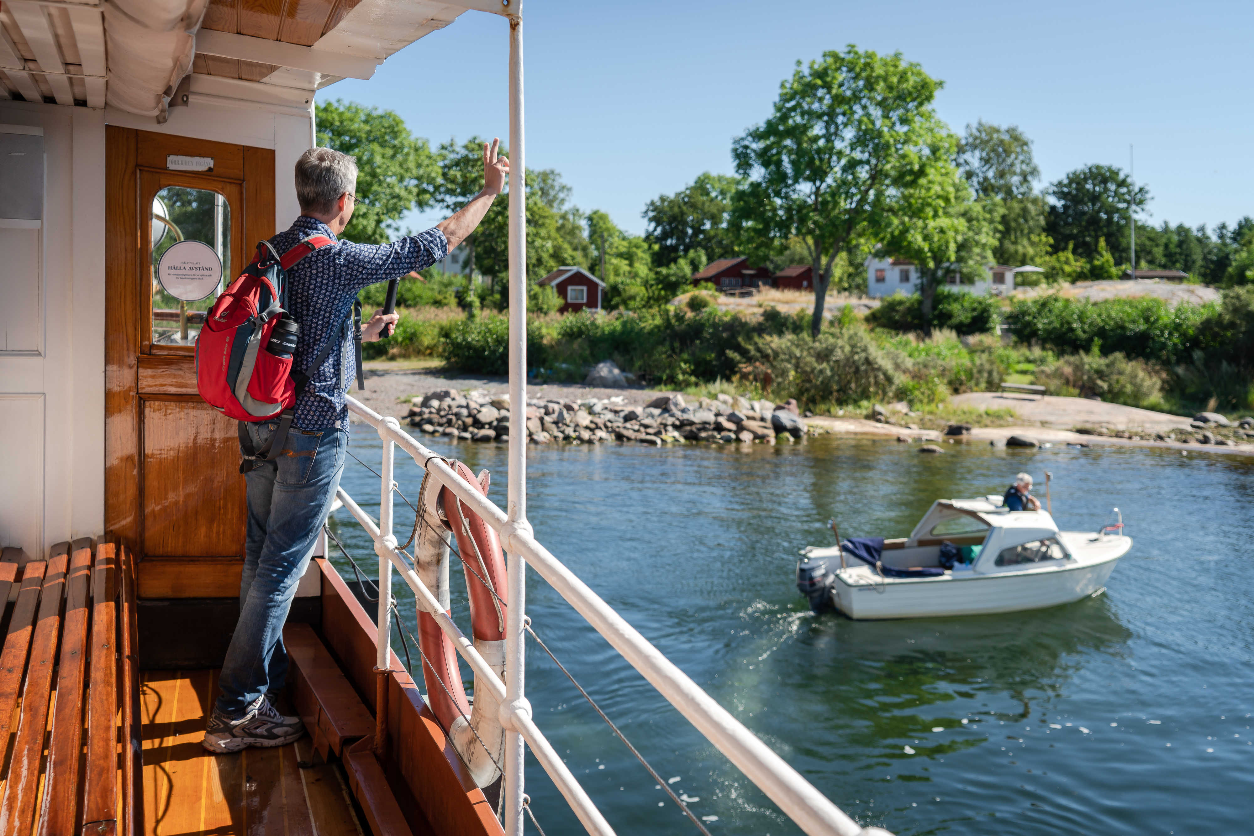 Vinkande man på ångbåten Blidösund med en ö med röda stugor i bakgrunden