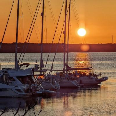 Gästhamn med båtar längs en brygga  i solnedgång. Orange himmel och blått hav