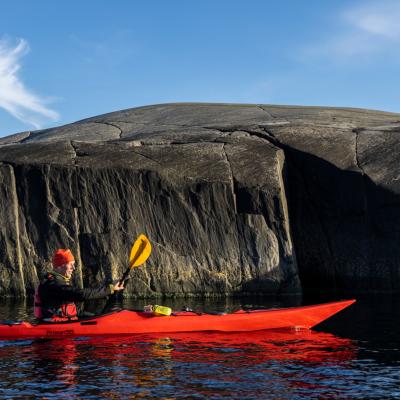 Paddlare i röd kajak i vattnet framför en kal och brant klippa