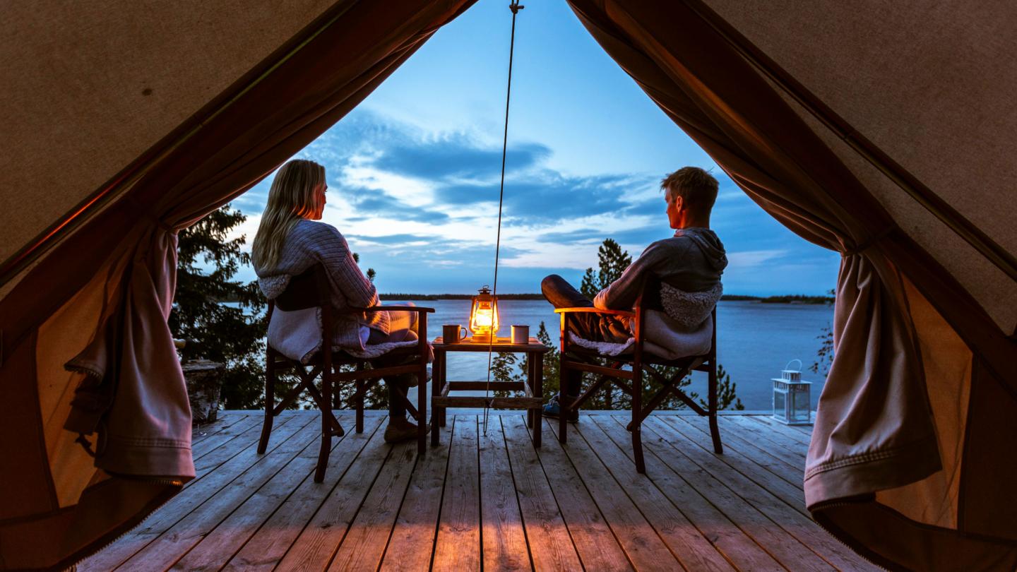 Par på glamping i skärgården sittandes på stolar framför tältet med utsikt över havet.