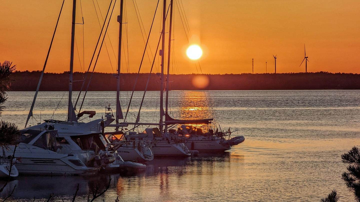 Gästhamn med vita båtar i solnedgången. Orange himmel och blått hav