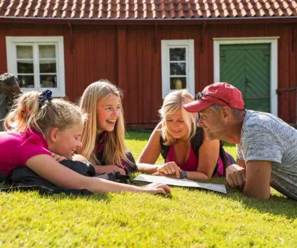 Familj som ligger i gräset och tittar på en ledkarta