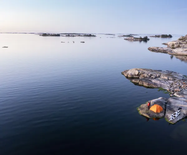 Drönarbild över ytterskärgården kring Norrpada. Blått hav, kajaker, kajakister och tält