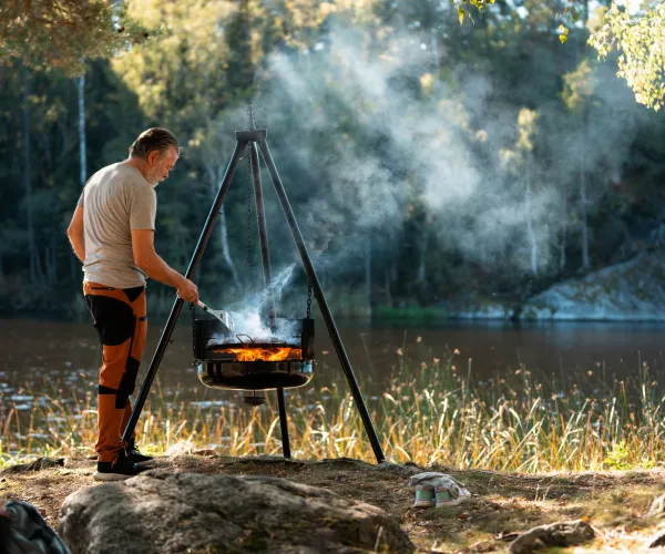 Man som grillar på en grill ute i naturen vid en sjö.